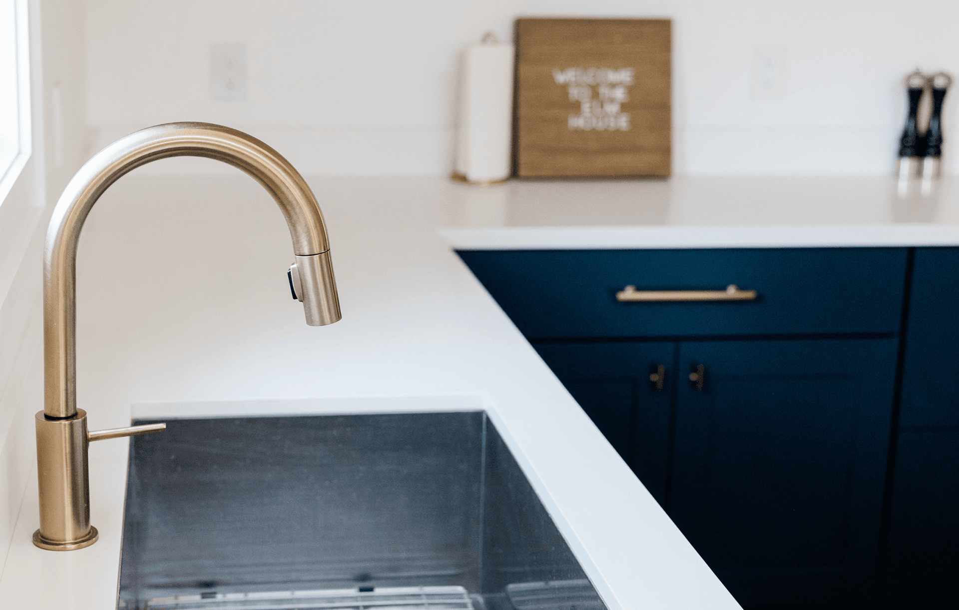 A modern kitchen sink with a brass faucet and deep navy cabinetry