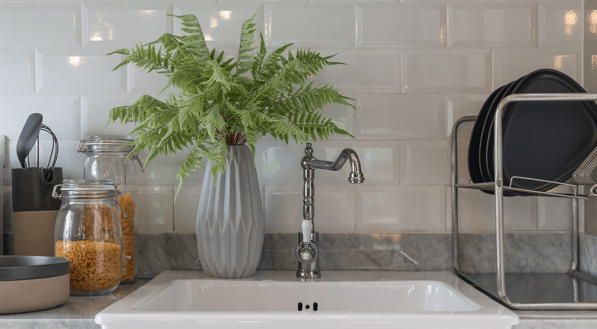 A tidy kitchen sink with a fresh fern, white subway tile, and marble counter